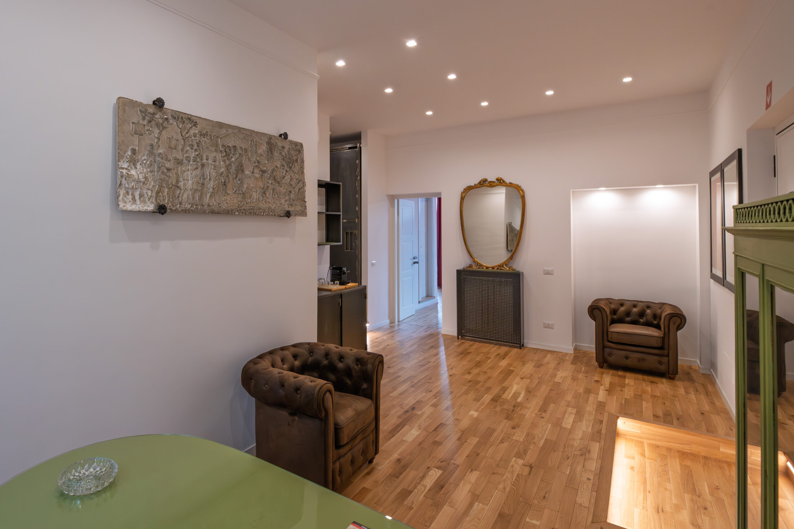 Soggiorno luminoso con poltrone chesterfield e specchio d'epoca nell'appartamento Effe9 a Roma